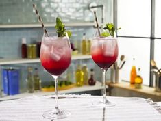 two wine glasses filled with red liquid and garnished with mint leaves, sitting on a table in a kitchen