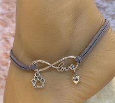 This anklet features an infinity charm with a silhouette paw charm. Attached to the infinity charm is gray leather straps. A gray bead and silver heart  bead dangle from the infinity charm.  This anklet detaches at the back of the anklet with a lobster claw latch and is size adjustable. Comfortable and versatile, it will lend itself to casual or formal events. All items are made in a smoke free environment. *If there is any issue with your anklet, please let me know so I can correct it. Thanks for visiting my shop!👣 Adjustable Anklets For Valentine's Day Gift, Columbia Tn, Leather Anklets, Infinity Charm, Infinity Love, Grey Beads, Ankle Bracelet, Gray Leather, Anklet Jewelry