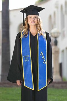 a woman wearing a blue and yellow graduation cap, gown and tassel standing in front of a building