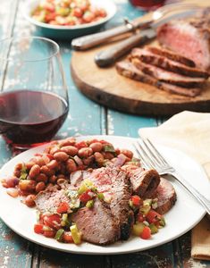 a white plate topped with meat, beans and veggies next to a glass of wine