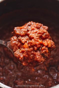 a ladle full of chili sauce with a spoon in it