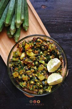 green beans and other vegetables in a glass bowl on a wooden cutting board with lemon wedges