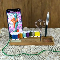 a cell phone sitting on top of a wooden stand filled with crafting supplies and thread