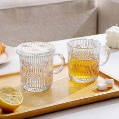 two glass mugs sitting on top of a wooden tray next to lemon slices and marshmallows