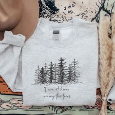 Discover your wilderness spirit with our Pine Tree Sweatshirt. This nature-inspired crewneck, featuring the heartfelt phrase "I am home among the trees" and a graphic of a pine tree forest, is the perfect nature lover gift for granola girls, camping enthusiasts, and hiking aficionados. Everything You Need to Know: 🧥 Sweatshirt Brand Gildan | Unisex Adult Sizing | 50% Cotton, 50% Polyester ⏳🚚 Production & Shipping All items are made-to-order. They will ship within 1-5 business days from one of Winter Crew Neck Tops For Adventure, Custom Print Crew Neck Top For Outdoor, Cricut Sweatshirt Ideas, Classy Tattoos, Granola Girl, Hiking Shirts, Branded Sweatshirts, Gifts For Nature Lovers, Nature Lover