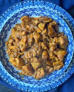 a blue and white plate topped with meat covered in gravy on top of a table