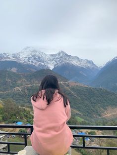 a woman sitting on top of a bench looking out at the mountains in the distance