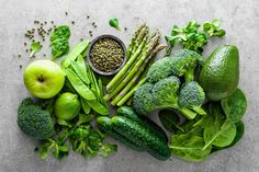 an assortment of fruits and vegetables laid out on a gray surface, including broccoli