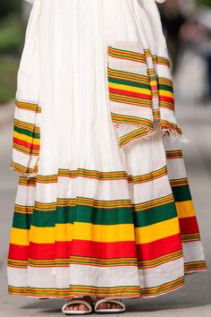 This Shimena Habesha dress is a true masterpiece that represents the pride and beauty of Ethiopia. The dress is made with high-quality Menen fabric, which adds a touch of elegance and sophistication to the overall design. The dress features a unique flag-inspired design, with green, yellow, and red stripes that run along the hem of the dress, representing the colors of the Ethiopian flag. The dress is also adorned with intricate patterns and embroidery, which adds a traditional touch to the mode Multicolor Dresses With Woven Motifs For Festivals, Multicolor Woven Motifs Dresses For Festivals, White Dress For Navratri, Traditional Drape Handloom Dress For Festivals, Handloom Dresses With Traditional Drape For Festivals, Multicolor Dress For Diwali Ceremonies, Multicolor Dresses For Diwali Ceremonies, Multicolor Dresses For Diwali And Traditional Ceremonies, Multicolor Handloom Dress With Traditional Drape