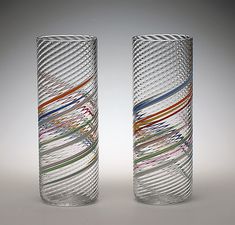 two tall glass vases sitting next to each other on a white surface with multicolored lines