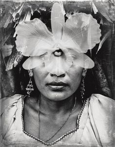 a black and white photo of a woman with flowers on her head in front of her face