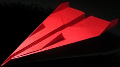 a red origami airplane sitting on top of a black surface in the dark