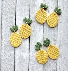 four yellow pineapples with green leaves are on a white wooden surface and one is made out of clay