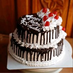 a three layer chocolate cake with white frosting and cherries on top, sitting on a plate