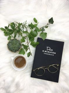 a book, glasses and potted plant sit on a white furnishing next to a cup of coffee