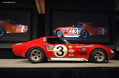 a red race car sitting on top of a stage next to two large screen screens