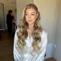 a woman with long blonde hair wearing a white shirt and flower in her hair is looking at the camera