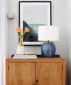 a blue vase sitting on top of a wooden cabinet next to a lamp and painting