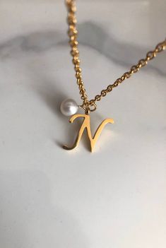 "Letter N necklace, set on a stainless steel ,golden color chain. Chain length 19'  With addition cost there is an option to add a white freshwater pearl, as a charm, next to the letter. 6 mm, white round pearl Kindly choose your option. Beautiful spiritual gift. Please make sure you to pay attention to the size of the pendant. I have added pictures next to 25 cent coin, and measurement tape.  Need a different length just write it to me in the \"message to the seller\" box of the order form. **L White Minimalist Initial Necklace As Gift, Minimalist White Initial Necklace For Personalized Gift, Elegant Hypoallergenic Charm Necklace With Initial Pendant, Elegant Hypoallergenic Initial Pendant Charm Necklace, Elegant Initials Necklace In Stainless Steel, White Minimalist Initial Pendant Necklace, Elegant Initials Stainless Steel Necklace, Minimalist White Initial Necklace, Elegant Stainless Steel Initials Necklace