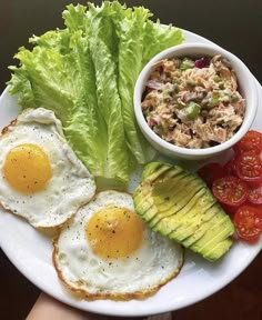 a plate with eggs, avocado, tomatoes and lettuce