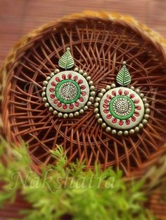 pair of green and red earrings sitting on top of a wicker basket next to a plant