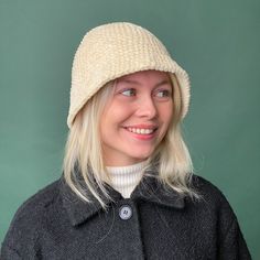 a woman with blonde hair wearing a white knitted hat and black coat, smiling at the camera