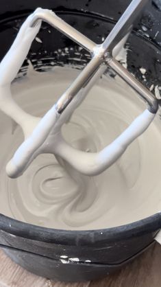 a whisk is being made in a black bowl with white icing on it