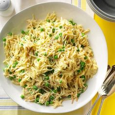 a white bowl filled with pasta and peas on top of a yellow table cloth next to silverware