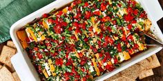 a casserole dish filled with cheese, tomatoes and spinach on top of crackers