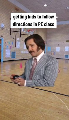 a man sitting on top of a basketball court holding a remote control in his hand