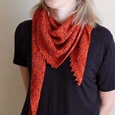 a woman wearing a black shirt and an orange crocheted shawl is standing in front of a white wall