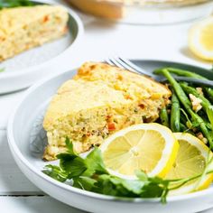 a white plate topped with green beans and lemon wedges next to a slice of quiche