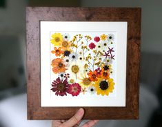 a person holding up a framed artwork with flowers on it