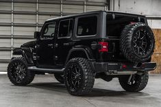 a black jeep parked in front of a garage door with the doors open and wheels off