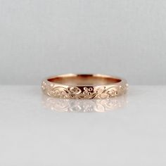 a gold wedding ring with an intricate design on the side, sitting on a white surface