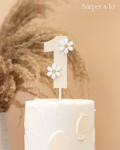 a white cake topped with a number one frosted in icing and daisies