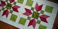 a quilted table topper with red and green stars on the center, sitting on a wooden floor