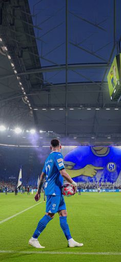 a soccer player is walking on the field with a ball in his hand and people watching from the stands