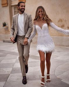 a man and woman are walking down the street in white dresses with feathers on them