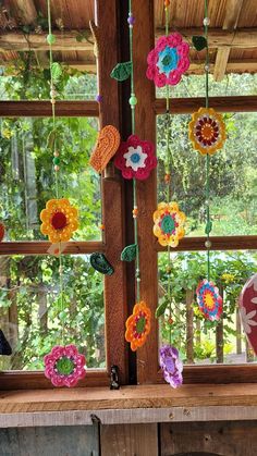 colorful crocheted flowers hanging from a window sill in front of a wooden structure