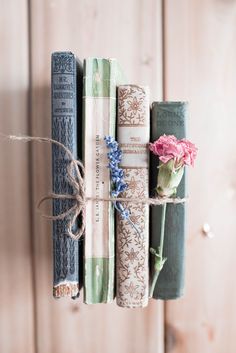 three books tied together with twine on top of each other next to a pink flower