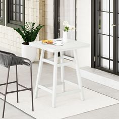 a white table sitting on top of a floor next to a chair and potted plant