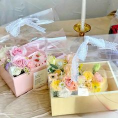 two boxes with flowers in them sitting on a table next to a candle and some candlesticks