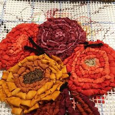 four different colored flowers sitting on top of a white cloth covered tablecloth with thread spools in the middle