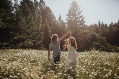 two children are playing in a field of flowers with their arms up to each other