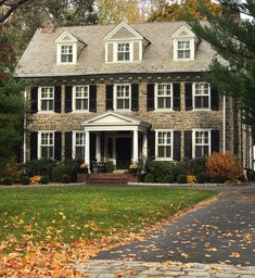 a large brick house with white trim and black shutters on the front door, surrounded by autumn leaves