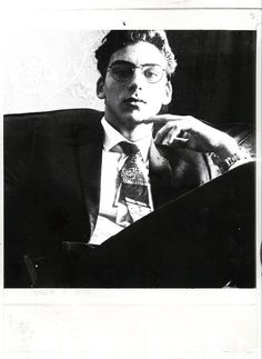 a black and white photo of a man with glasses sitting in front of a book