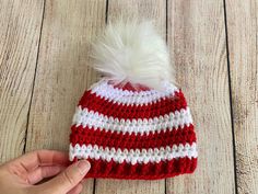 a hand is holding a red and white knitted hat with a pom - pom