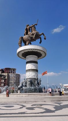 a statue of a man riding a horse in front of a fountain with people walking around it