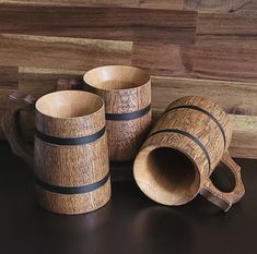 three wooden mugs and two cups on a black counter top with wood planks in the background